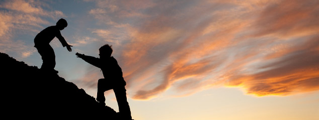 Silhouette of a boy giving another boy a helping hand